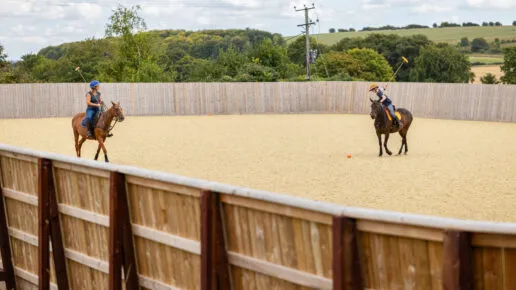 Two horses being ridden on a Tomley Projects outdoor equestrian arena with timber kickboards