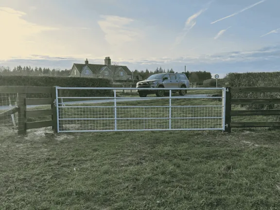 A metal gate with mesh at the bottom to protect horses hooves and legs from getting caught